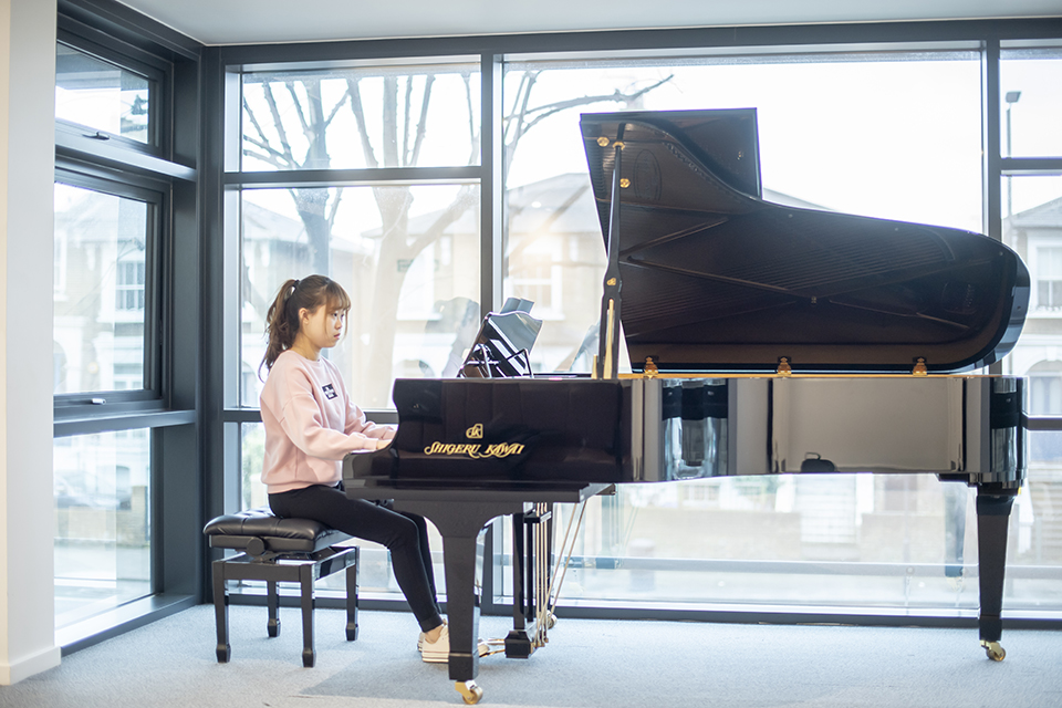 A female student practising on a piano in a well-lit room.